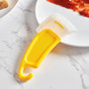 A yellow silicone kitchen scraper tool is shown on a white marble surface next to a plate with tomato sauce.