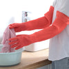 A person wearing bright orange silicone dishwashing gloves is washing items in a white bowl.