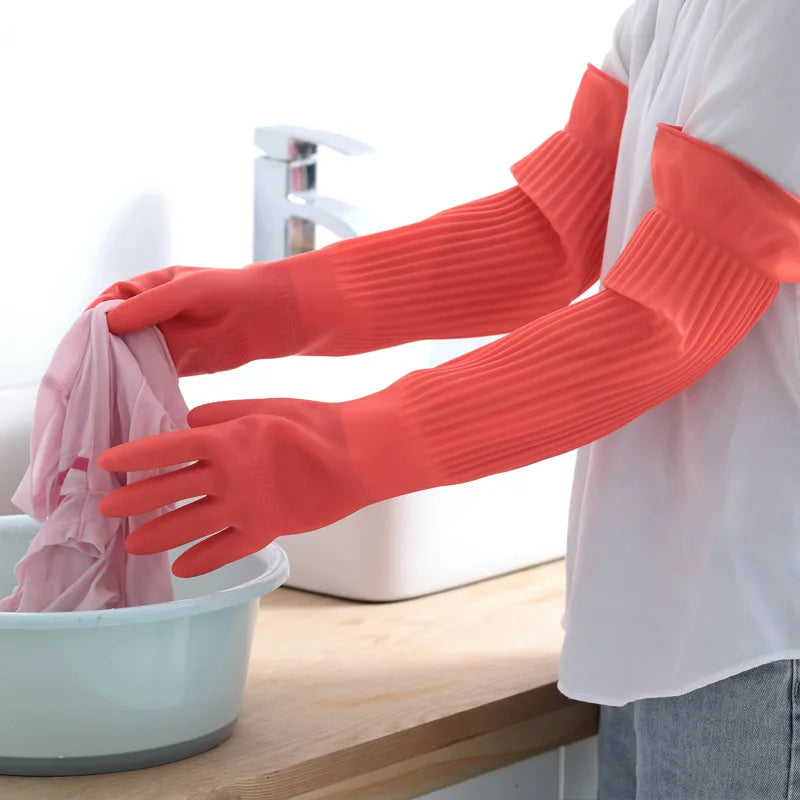 A person wearing bright orange silicone dishwashing gloves is washing items in a white bowl.