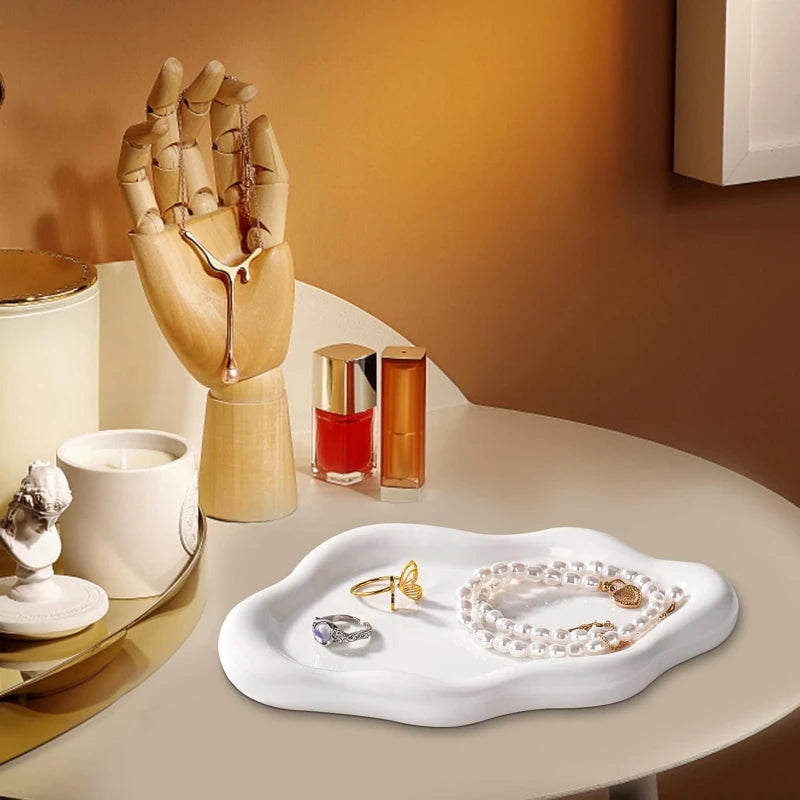A white jewelry organizer tray holds gold and pearl jewelry next to various cosmetic bottles on a light surface.