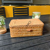 A handwoven rattan storage basket with a lid resting on a dark wooden surface.