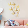 Gold glitter butterfly wall stickers displayed on a light pink wall above a sofa.