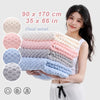 A woman holds a stack of thickened microfiber bath towels in various pastel colors and textures.