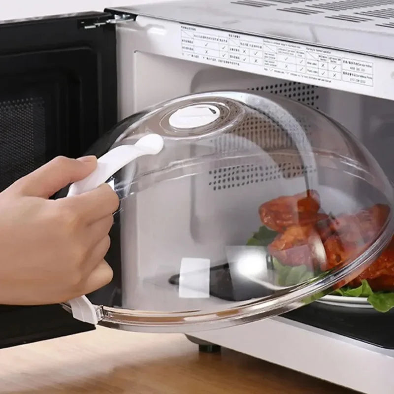 A hand is lifting a transparent splash-proof oven cover with a handle from an oven interior.