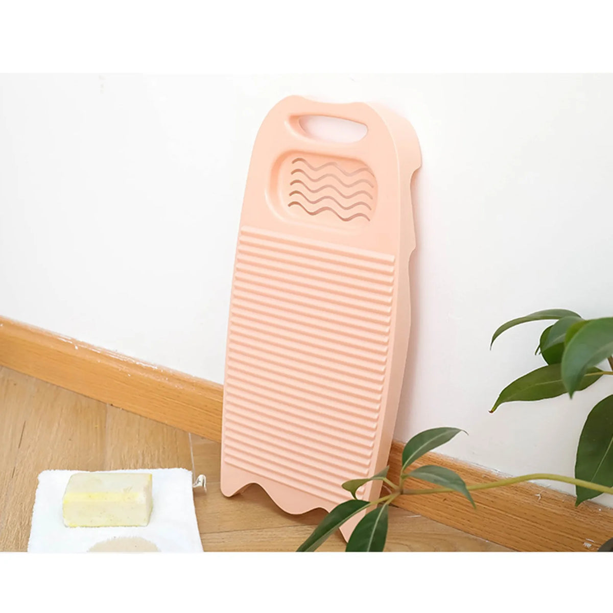 A light peach-colored thickened washboard for delicate laundry is shown next to a piece of yellow soap on a wooden surface.