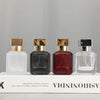Four glass perfume bottles in various colors and finishes displayed on a white box.