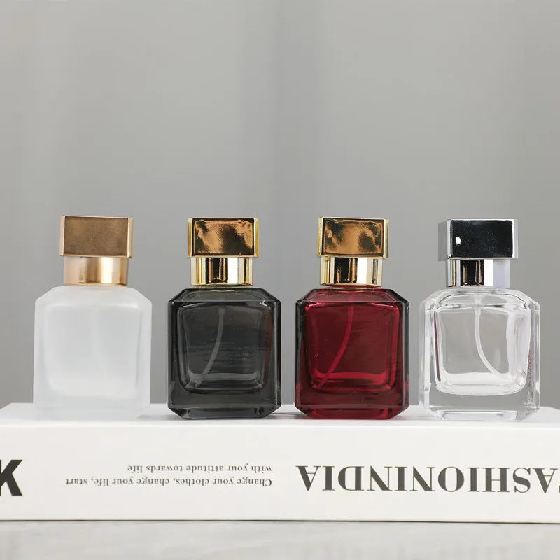 Four glass perfume bottles in various colors and finishes displayed on a white box.