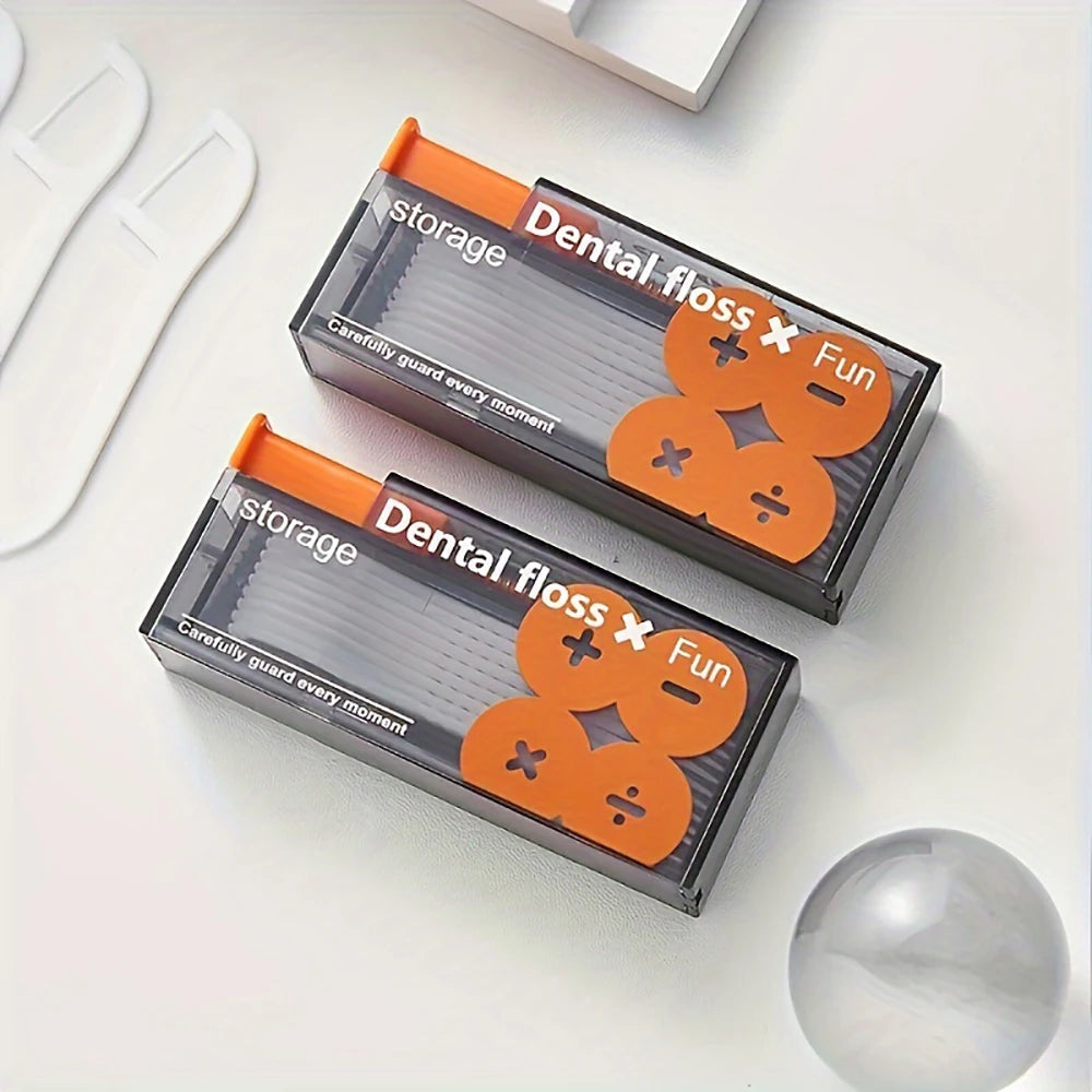 A black storage box for dental floss with an orange dispenser and a silver ball on a white surface.