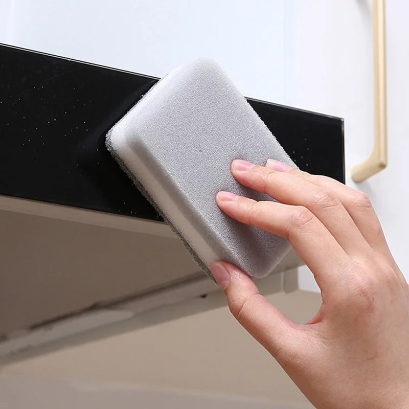A hand is using a gray double-sided cleaning sponge wipe on a black shelf or surface.