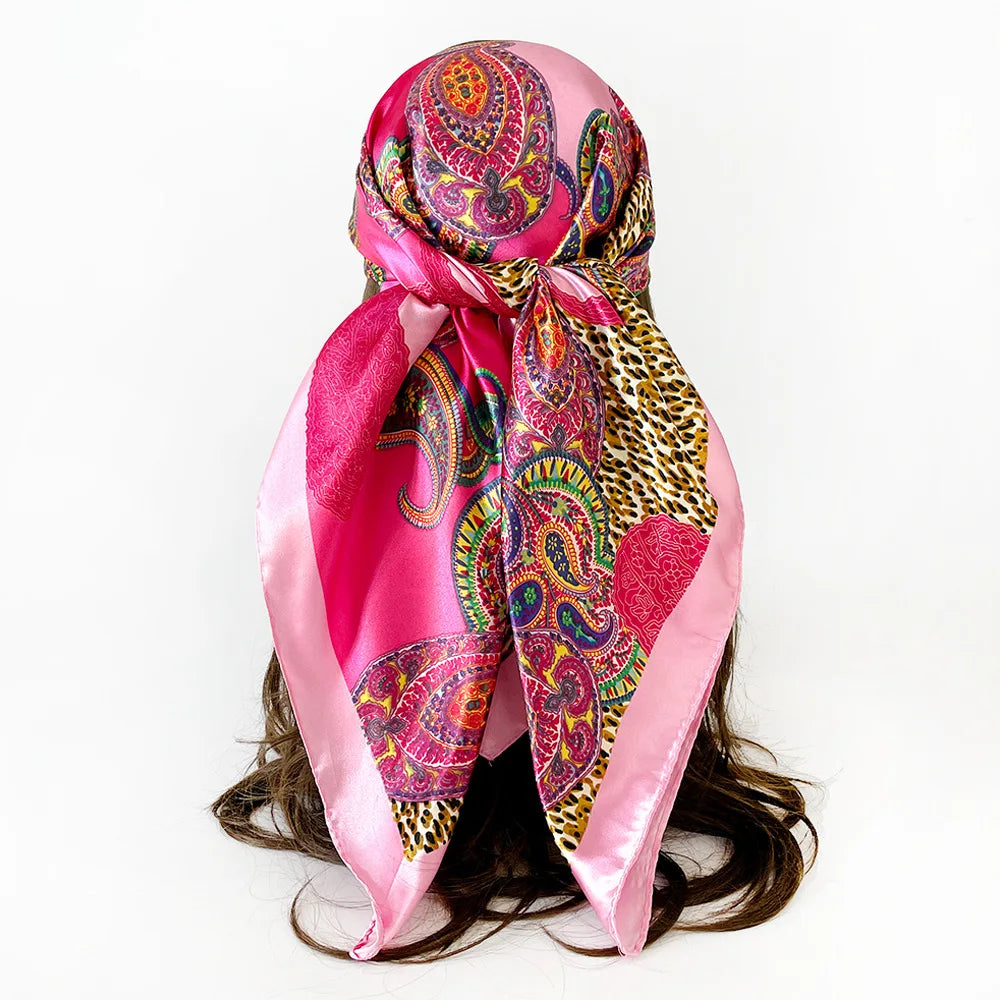 A vibrant pink scarf featuring a paisley print with leopard spots and colorful patterns tied around a dark hairstyle.