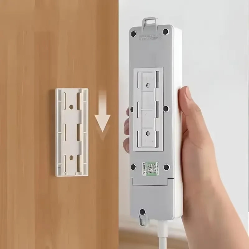 A white self-adhesive desktop cable organizer holder is shown being applied to a wooden door surface.