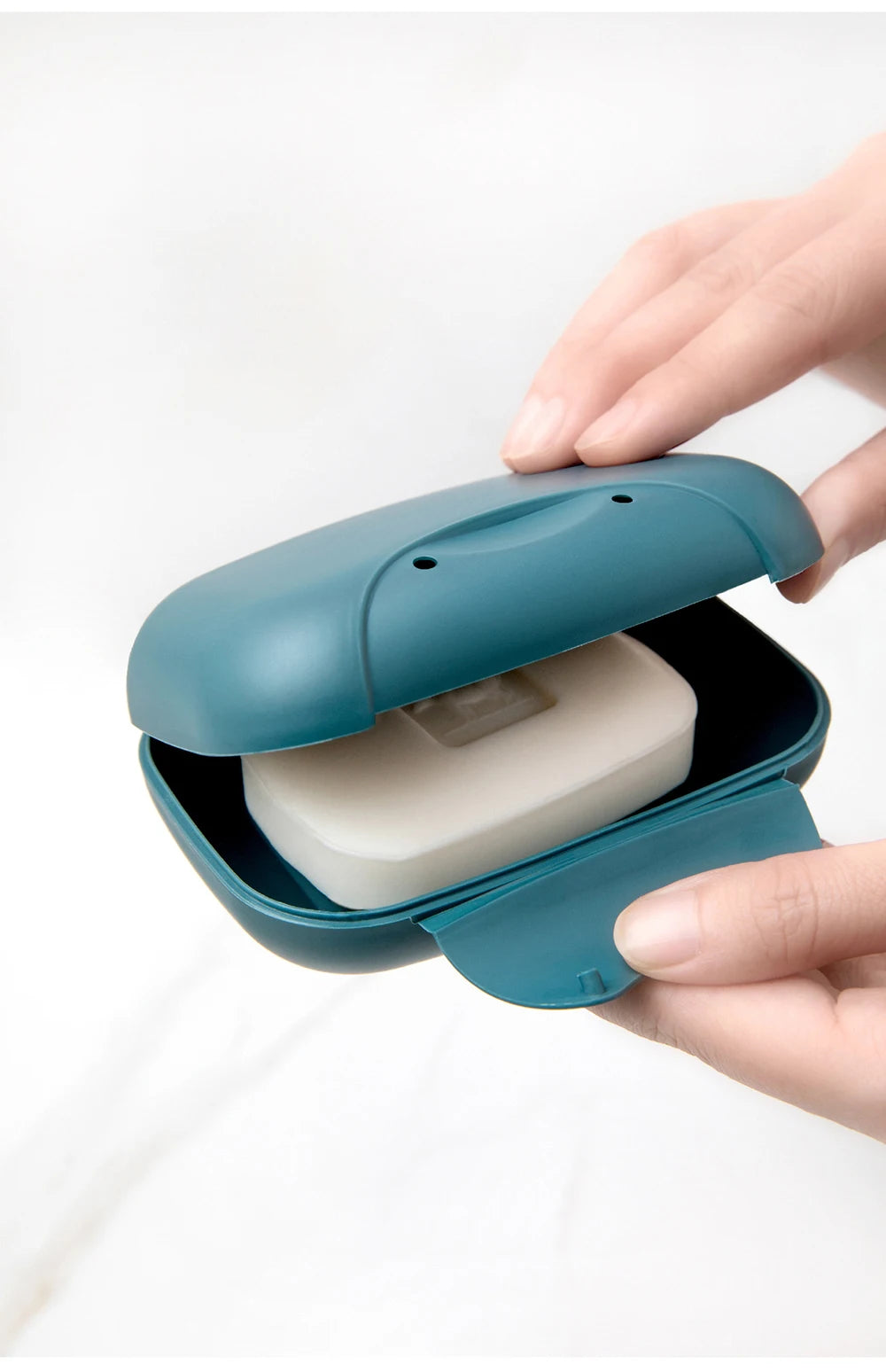 A hand opens a teal portable travel soap box to reveal a white bar of soap.
