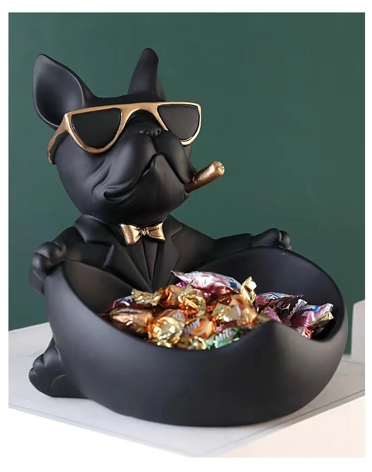 A black French bulldog sculpture wearing sunglasses sitting in a bowl filled with coins and snacks.