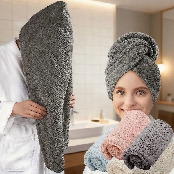 A woman is holding a gray microfiber hair drying towel wrap and several rolled towels in a bathroom setting.