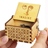 An antique wooden hand crank music box with a lid featuring the word IMAGINE is held in a person's hand.