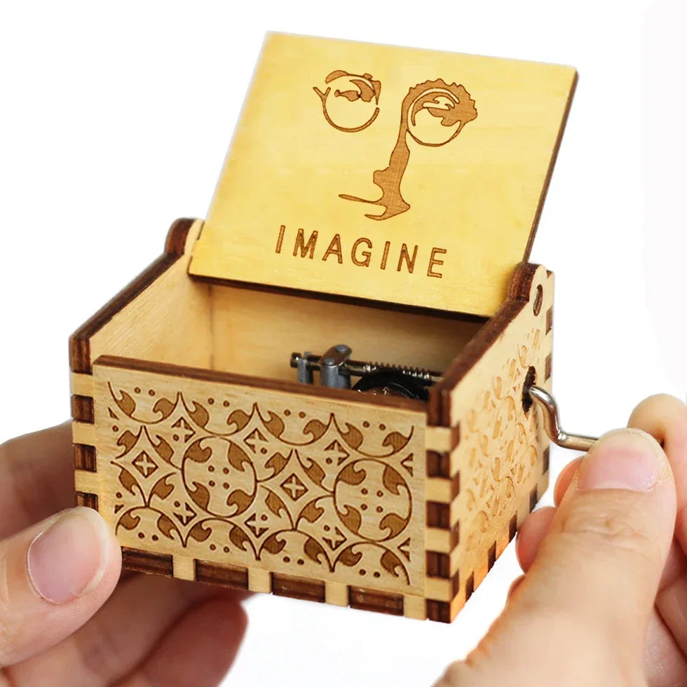An antique wooden hand crank music box with a lid featuring the word IMAGINE is held in a person's hand.