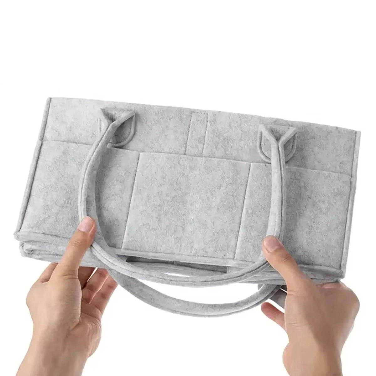 Une main tient un organisateur de couches en feutre gris avec des poignées.