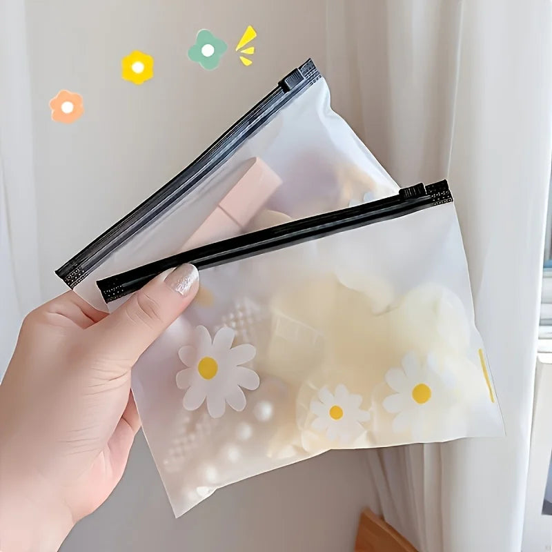 A hand holds a clear plastic zipper storage bag with a white daisy pattern, against a white background.