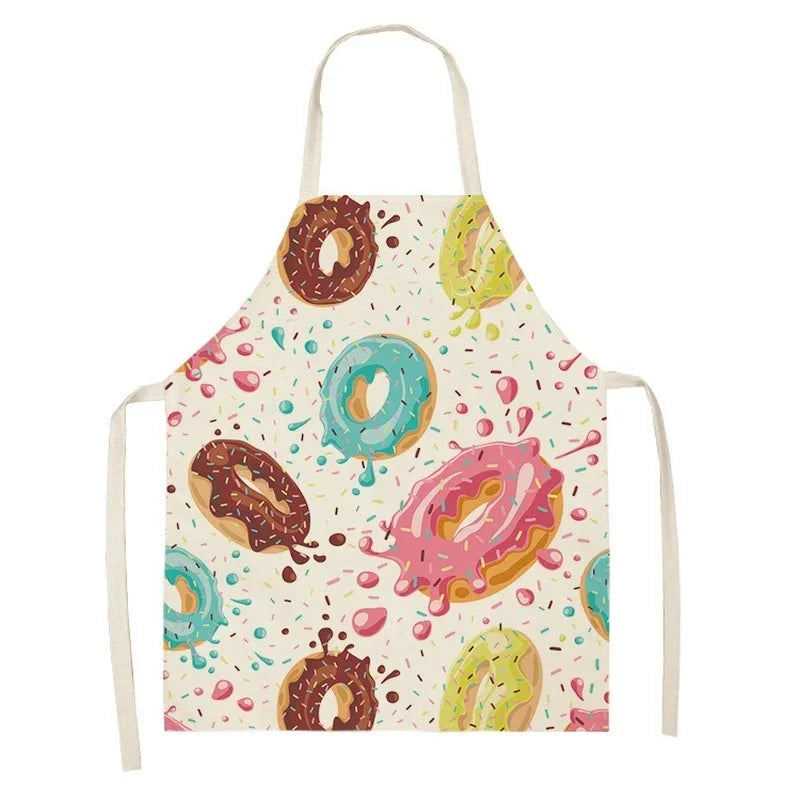 A white linen apron with a colorful donut print featuring pink, green, and brown icing on a light background.