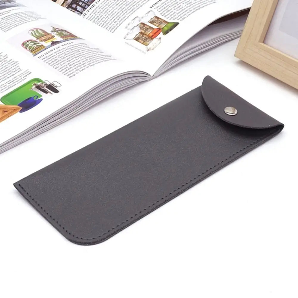 A dark gray PU leather eyewear case or glasses bag lying on a white surface next to an open magazine.