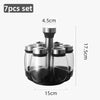 A set of seven clear glass spice jars with black lids and a rotating dispenser top, shown in a product photo.