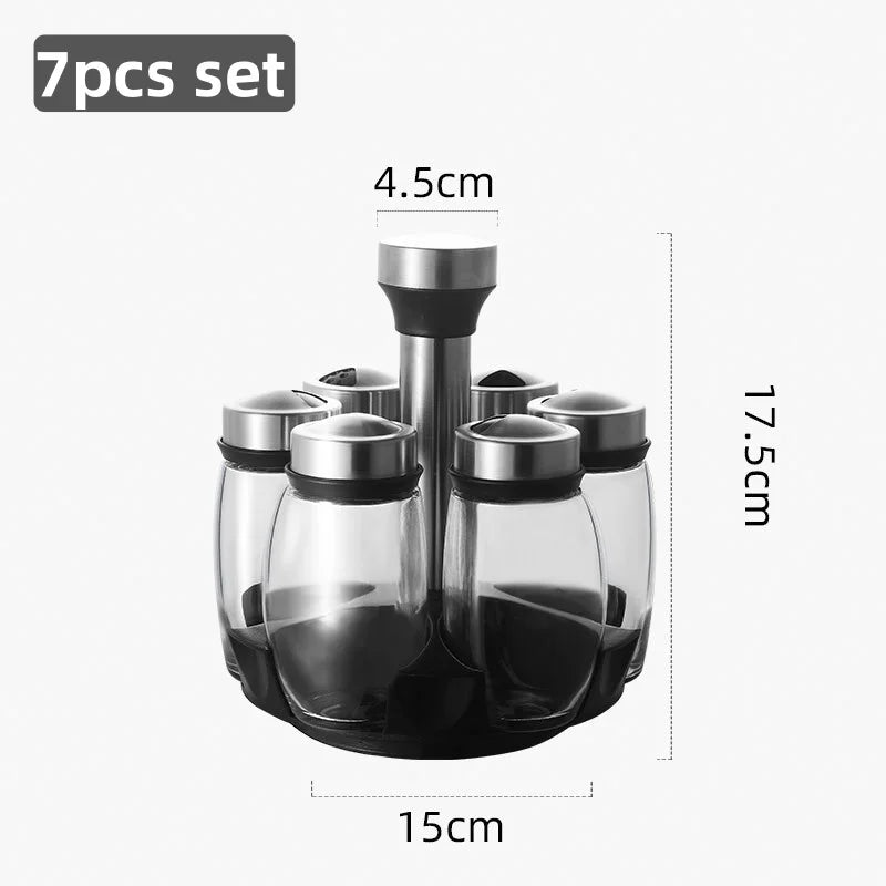 A set of seven clear glass spice jars with black lids and a rotating dispenser top, shown in a product photo.