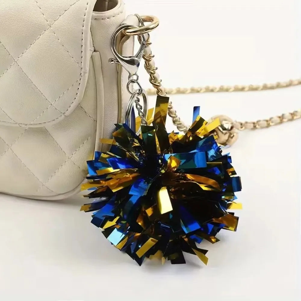 Goldkette mit dunkelblauem und goldenem Pom-Pom-Anhänger an einer hellbeigen gesteppten Ledertasche.
