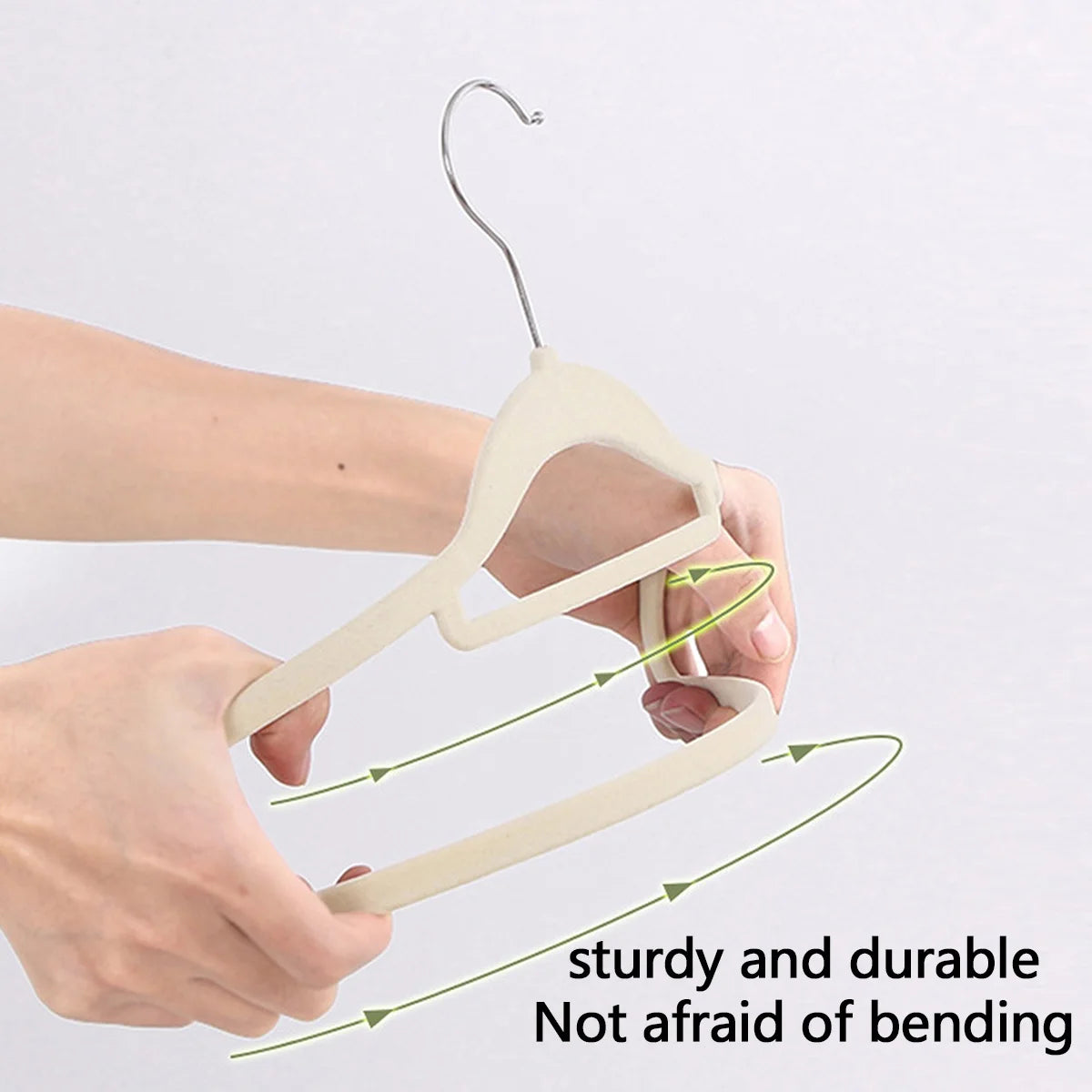A pair of light beige velvet slim hangers being held by a hand, demonstrating their sturdy and durable bending capability.
