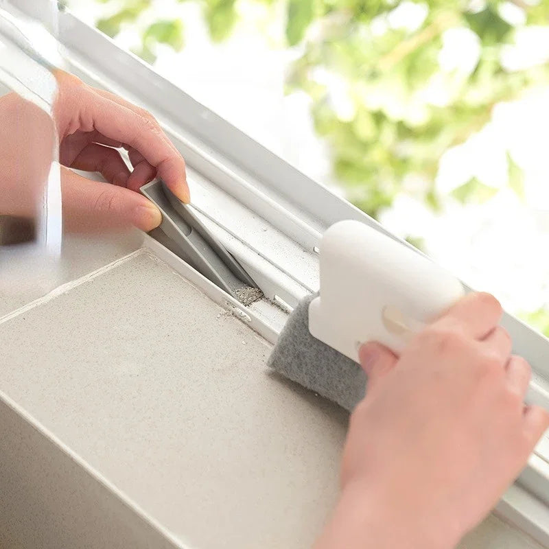 Una mano usa un cepillo de limpieza para limpiar una rendija de la ventana con una herramienta blanca.