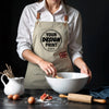 A person wearing a beige apron is shown holding a bowl and wooden tools on a dark surface.