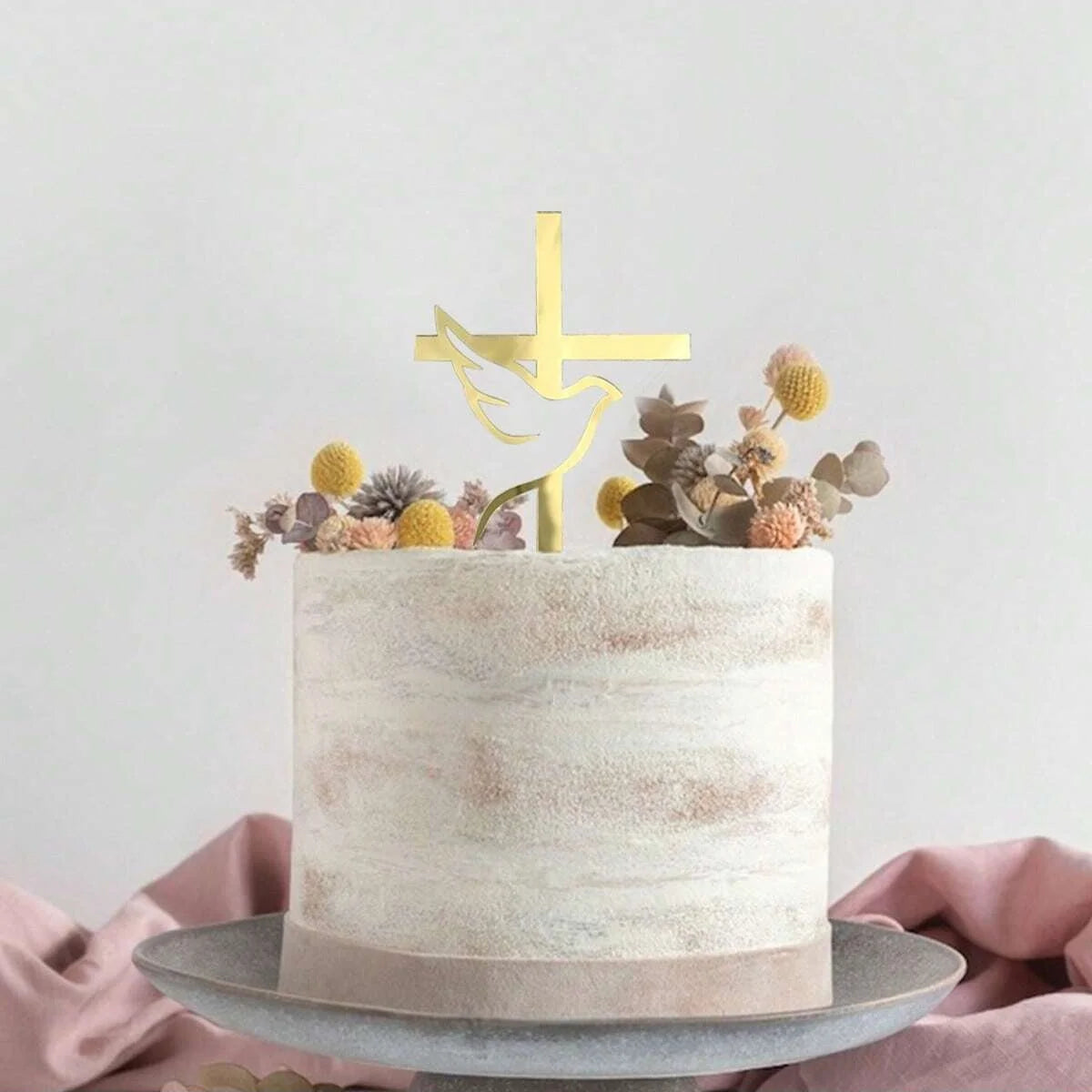 A round, light beige cake decorated with gold acrylic cross toppers and dried floral elements.