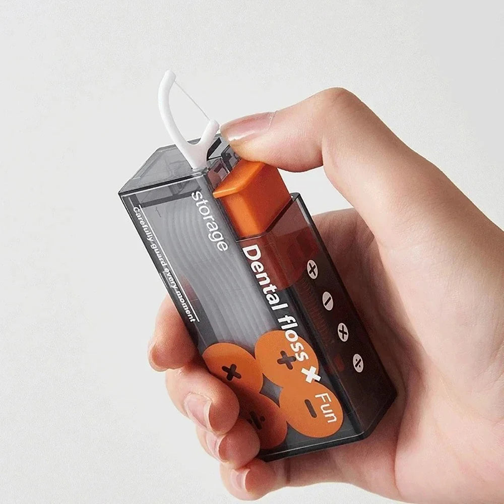 A hand holds a portable automatic floss storage dispenser with an orange cap and clear container.