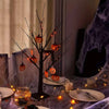 Dunkler Birkenbaum mit orangefarbenen LED-Lichtern und Halloween-Dekorationen auf einem Tisch.