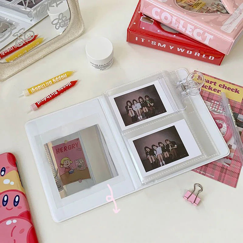 Un álbum de fotos blanco de 64 bolsillos para coleccionables junto a una caja rosa y otros artículos de manualidades.