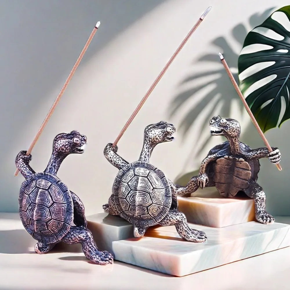 Trois petites figurines de tortues en métal avec des bâtons de bambou sont exposées sur une surface de marbre blanc.
