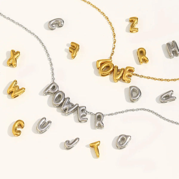 A collection of gold and silver 3D bubble letter alphabet necklaces displayed on a white background.