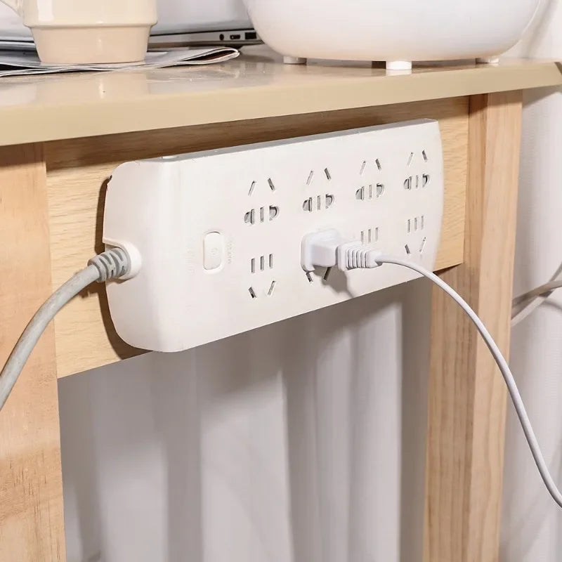 A white electrical outlet with multiple adhesive hooks is mounted on a wooden cabinet surface.