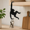 Black silhouette of a monkey hanging from a key chain on a wooden kitchen shelf