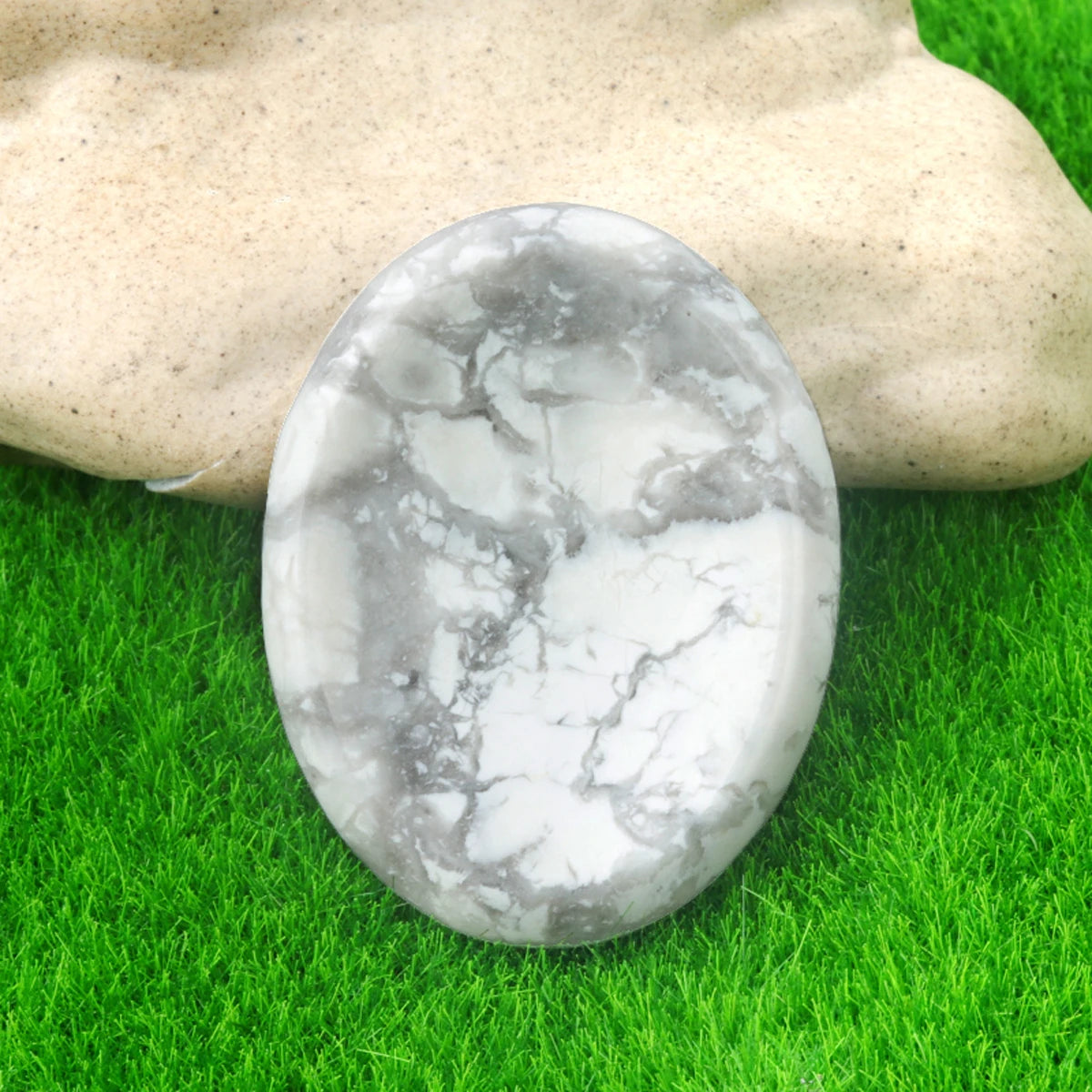 A smooth, oval piece of white and gray marbled quartz stone resting on vibrant green grass.