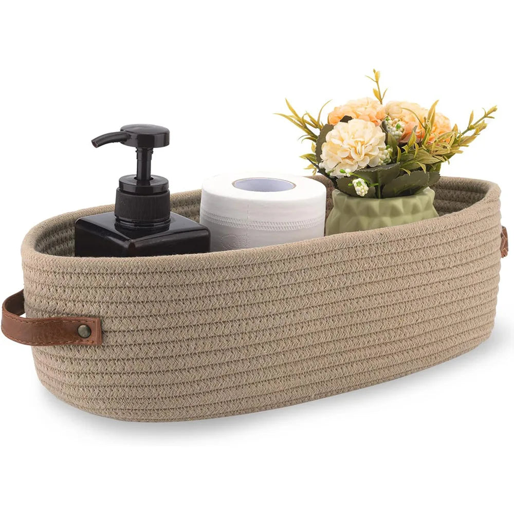 A woven cotton storage basket holds a black pump dispenser and a roll of white paper towels next to a bouquet of orange flowe