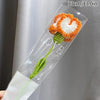Bouquet de fleurs de carnation en coton fait main avec des pétales orange et blanc et une tige verte dans une gaine en plasti