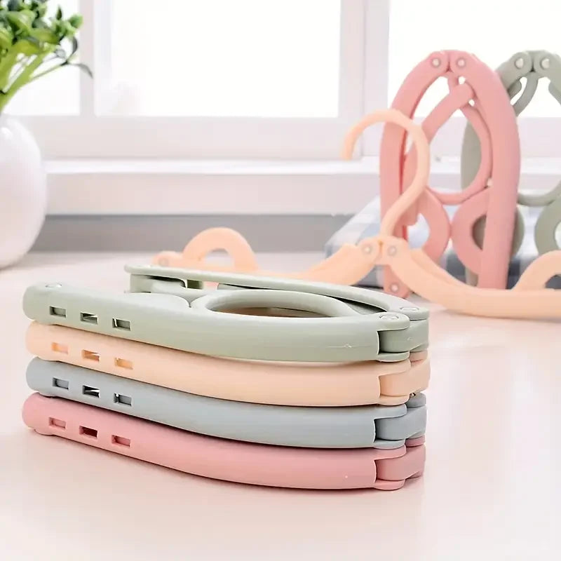 A stack of pink, beige, and green portable foldable clothes hangers on a white surface.