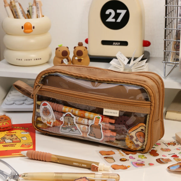 A brown transparent pencil pouch is shown next to various art supplies and a yellow box.