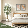 An artificial indoor olive tree in a white pot decorates a bedroom setting with natural light.