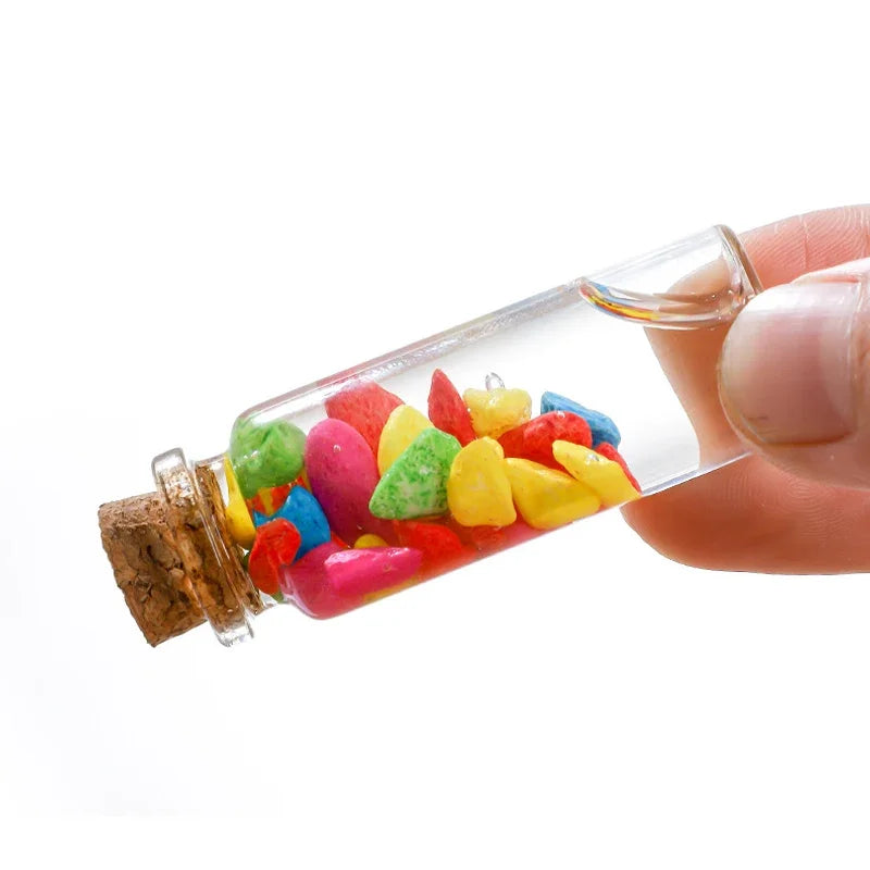Une main tient un flacon de potion en verre rempli de perles de verre colorées et d'un bouchon en liège.