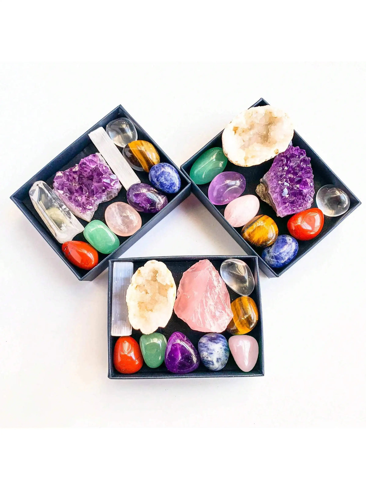 A collection of various colored natural crystals arranged in black square dishes for meditation and decor.