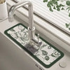 A modern chrome faucet mounted on a dark green mat in a kitchen sink.