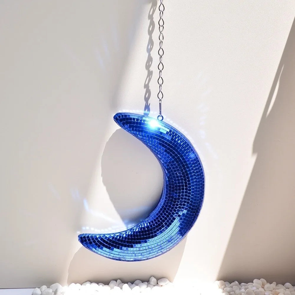 A bright blue mosaic moon pendant hangs against a white wall, casting a shadow.