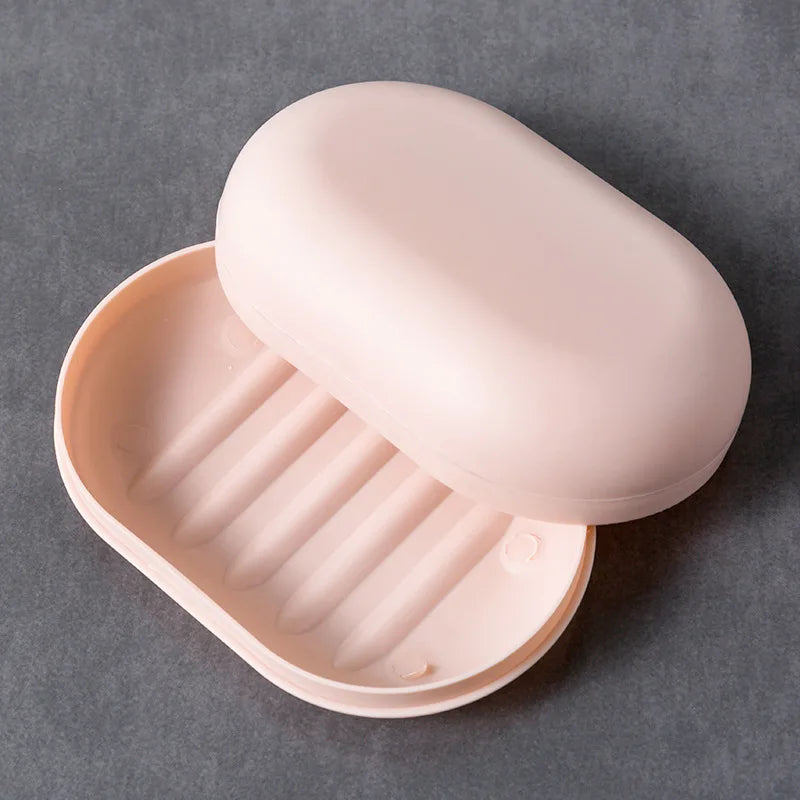 A pink portable soap holder with a lid is shown, featuring a ribbed tray for holding soap in a bathroom or travel setting.