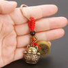 A vintage gold-tone lucky cat keychain with a red yarn tassel and gold coin charm held in a hand.